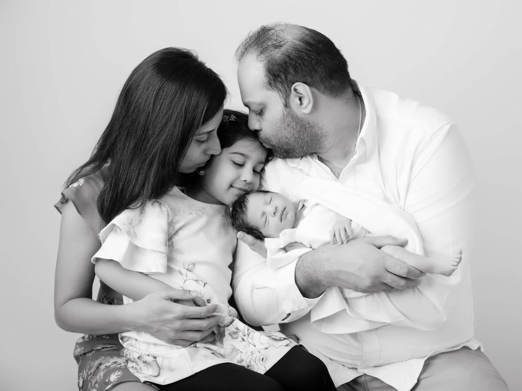 Studio portrait of a mum, dad, toddler and baby with parents kissing toddler. Juliette Scott photography in Perth